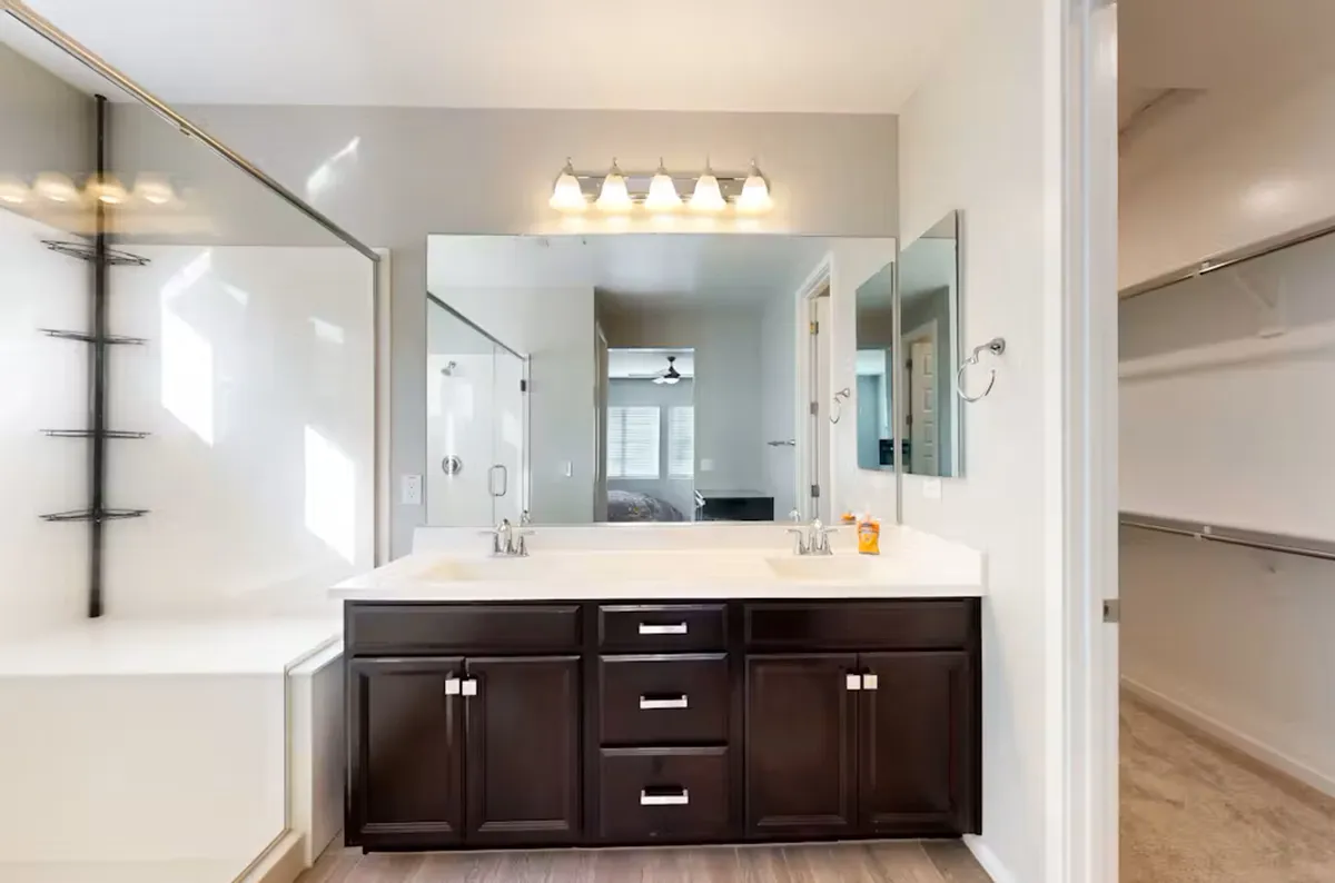 A serene bathroom with a double sink vanity, large mirror, walk-in shower, and a bathtub. The layout is spacious and luxurious, designed for self-care and relaxation after a long day.