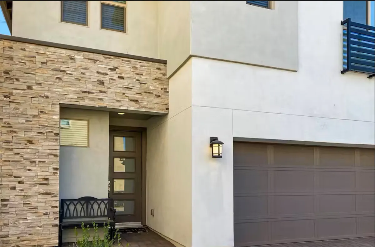 An inviting front exterior view featuring a stone facade, a welcoming front door, a bench, and attractive landscaping. The scene implies a sense of arrival, community, and neighborly connection.
