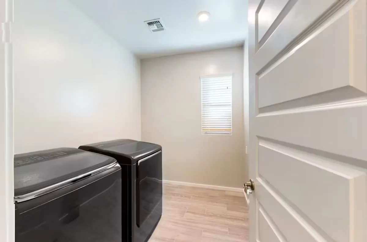 This image presents a well-lit, neatly organized laundry room featuring two modern black washing machines placed side by side beneath a window with blinds. The space is clean, uncluttered, and functional, signaling the ease and practicality of daily laundry care.