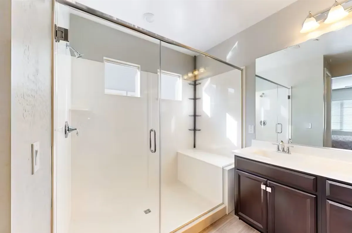 A modern bathroom with a glass shower enclosure, double sink vanity, and large mirrors. Morning light pours through the windows, illuminating the fresh and inviting space, ideal for self-care routines.