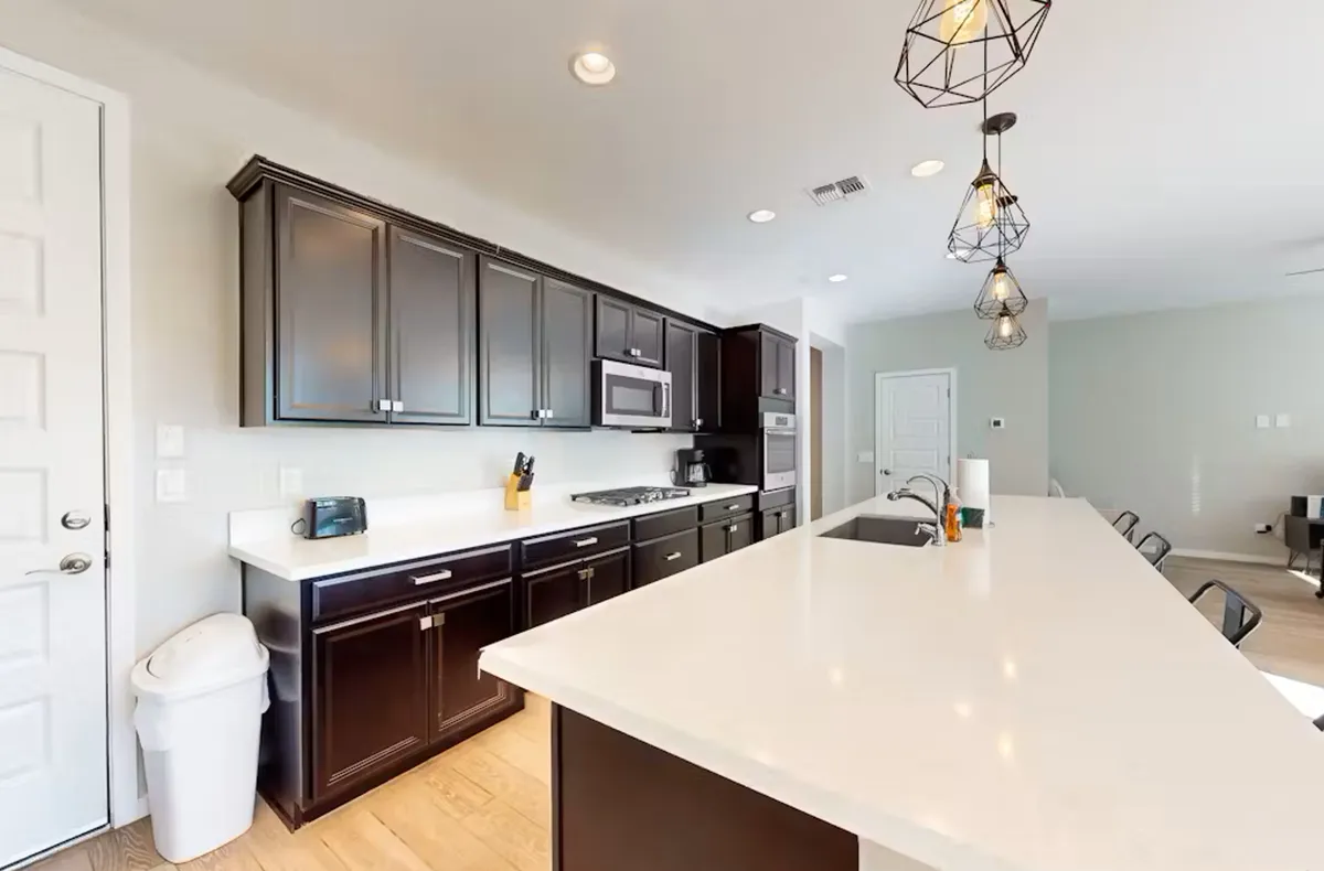 This view spotlights a spacious kitchen island with ample countertop space, warm lighting fixtures, and modern cabinetry. The arrangement is conducive to meal prep, casual dining, or informal gatherings, underscoring a sense of everyday ease and functionality.
